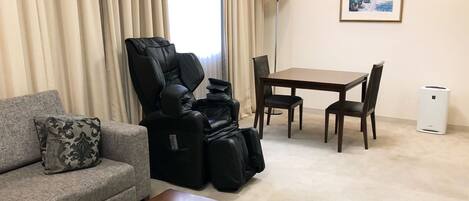 Una sala de estar con sofá, sillón de masaje, mesa de comedor con sillas, lámpara y un cuadro en la pared.