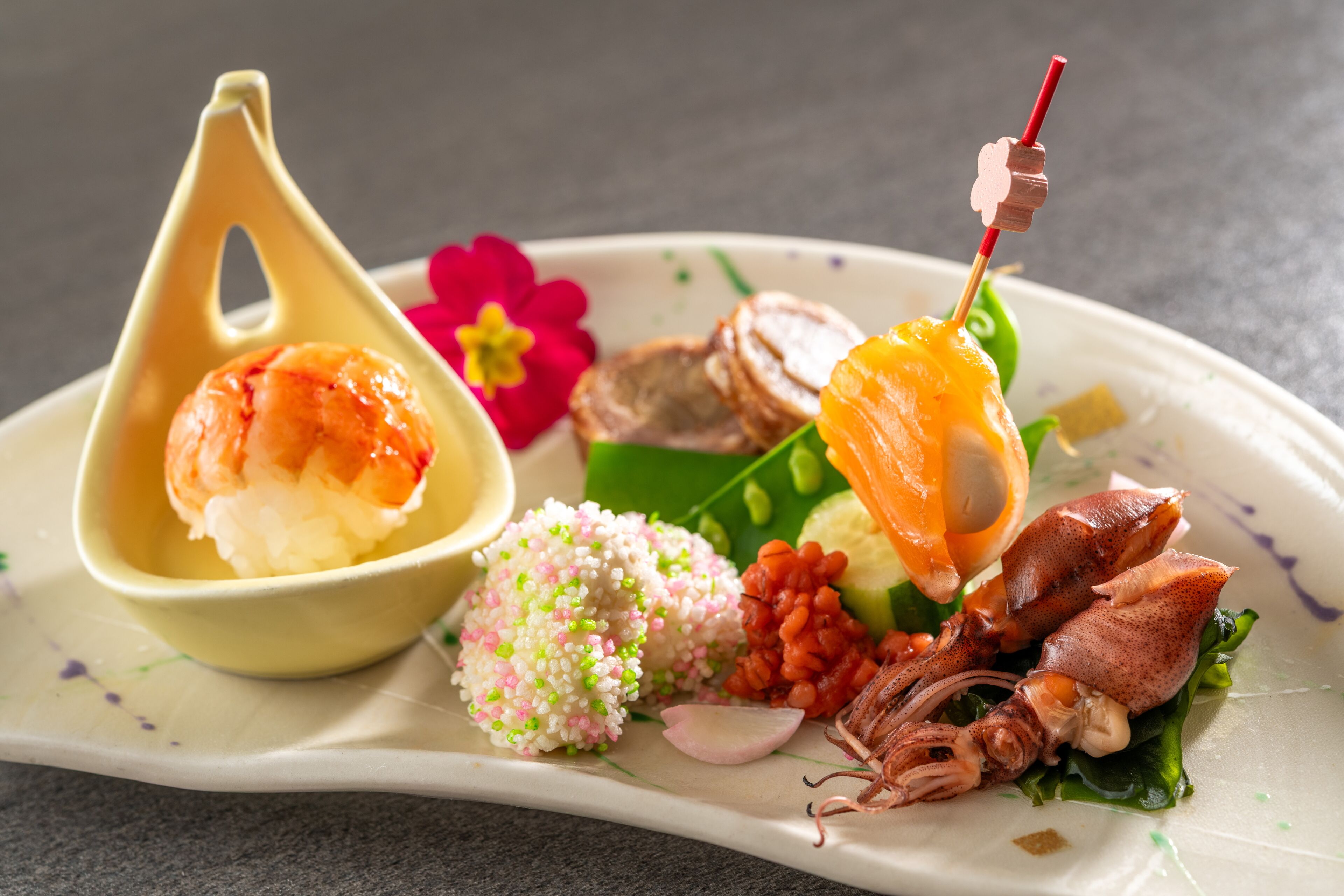 Une assiette contenant divers fruits de mer, notamment des crevettes, des calamars et peut-être aussi des œufs de poisson, disposés sur une assiette blanche ornée de motifs floraux.