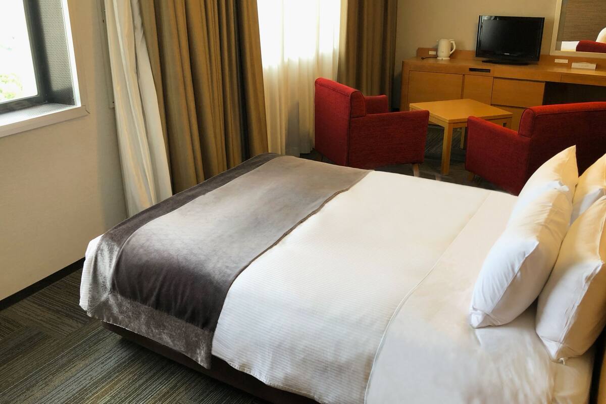 A hotel room with a large bed, a desk with a television, and red chairs.