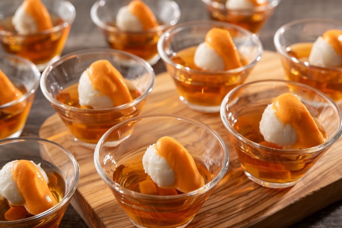 Una serie de vasos de vidrio transparente con un postre y cobertura caramelizada, servidos sobre una tabla de madera.
