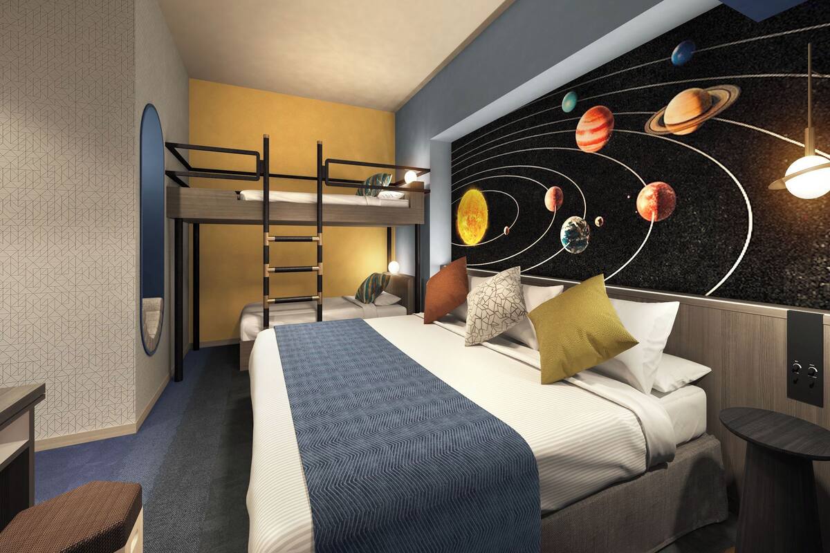 A room with bunk beds, a bed with pillows, a wall mural of planets, and a desk with a lamp.