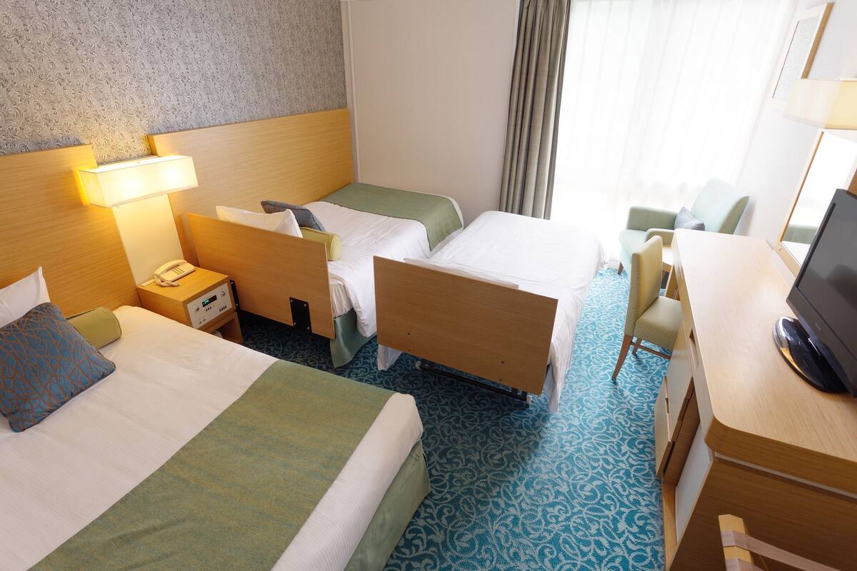 A hotel room with two beds, a desk, a chair, a TV, and a phone on the nightstand.