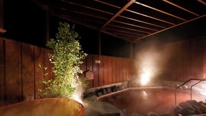 Zona de baños termales con estructura de madera, rocas y un banco de bambú.