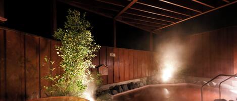 A hot spring bath area with a wooden structure, rocks, and a bamboo bench.