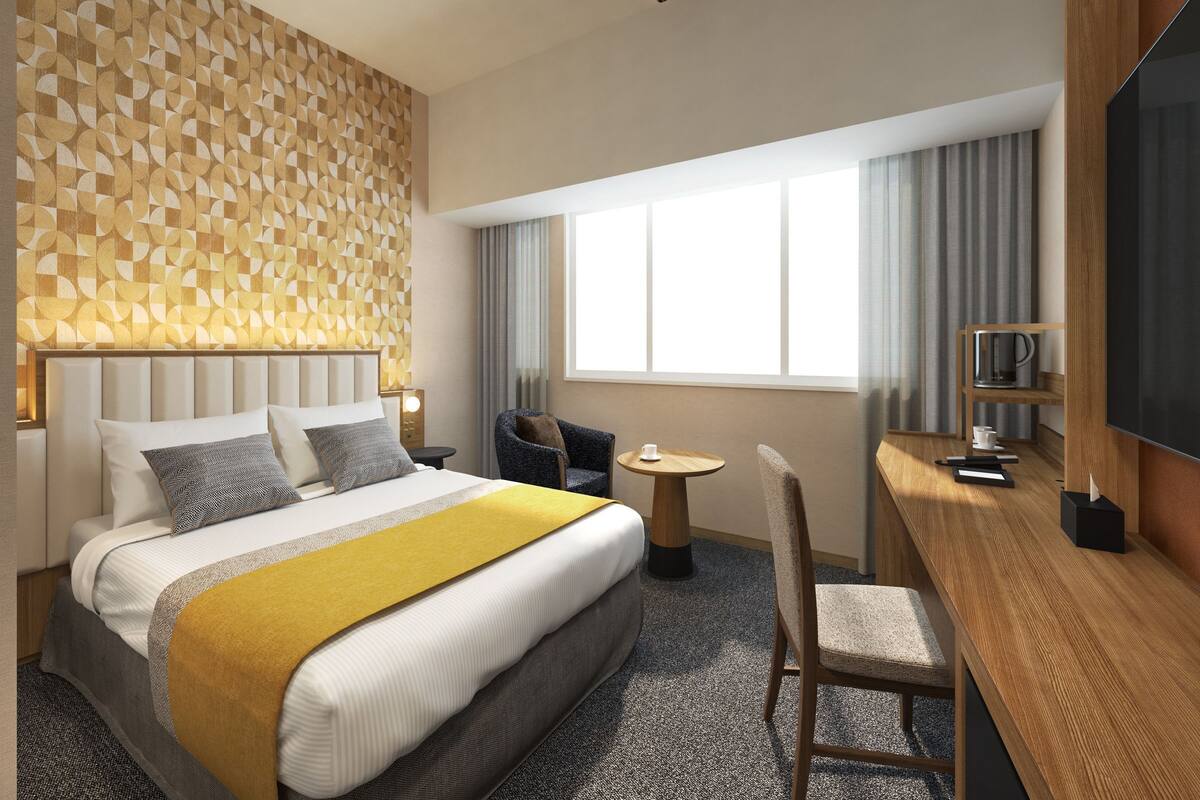 A hotel room with a bed, a desk, a chair, a TV, and a window with curtains.