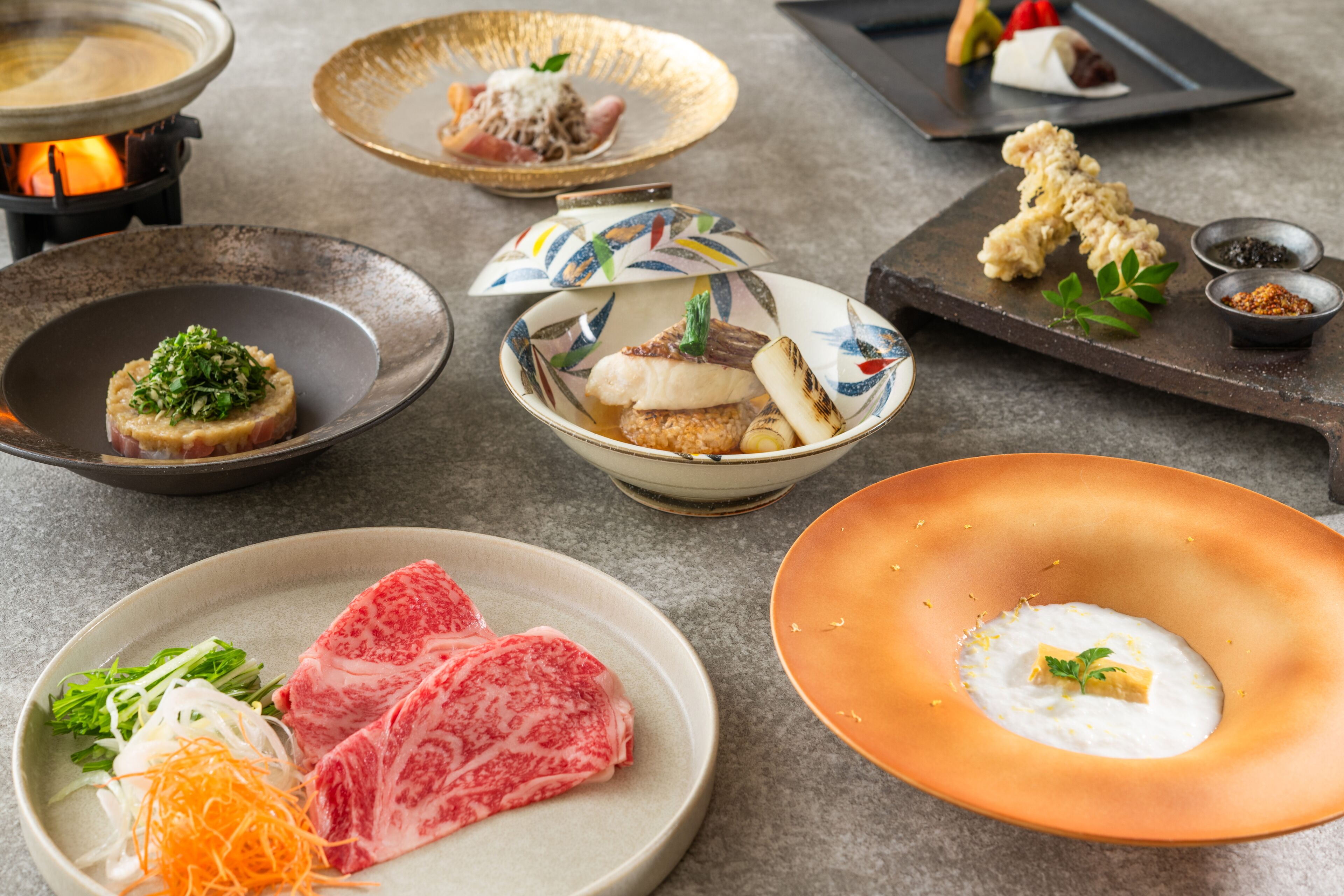 A variety of dishes including raw meat, vegetables, and a bowl of soup.