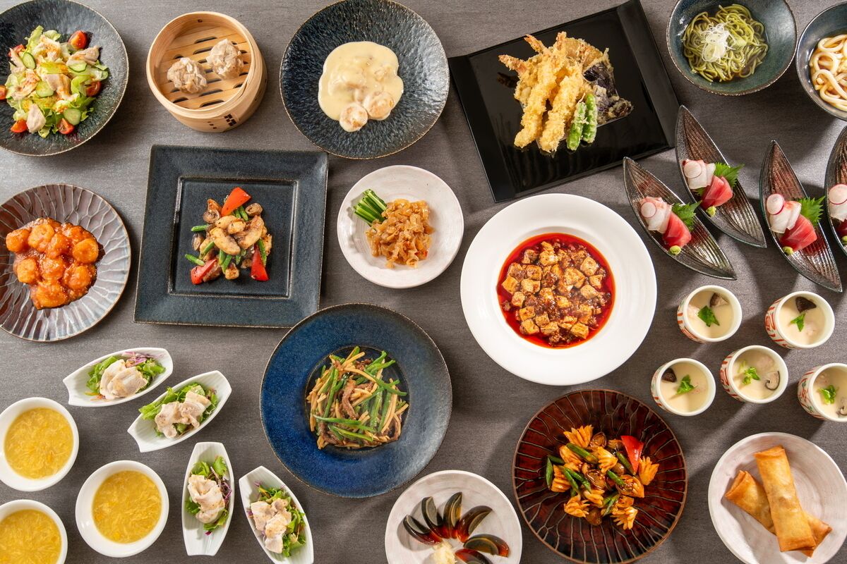 A variety of dishes on a table, including sushi, dumplings, and stir-fried vegetables.