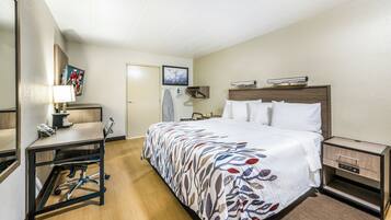 A hotel room with a bed, a desk, a chair, a wardrobe, and a mirror.