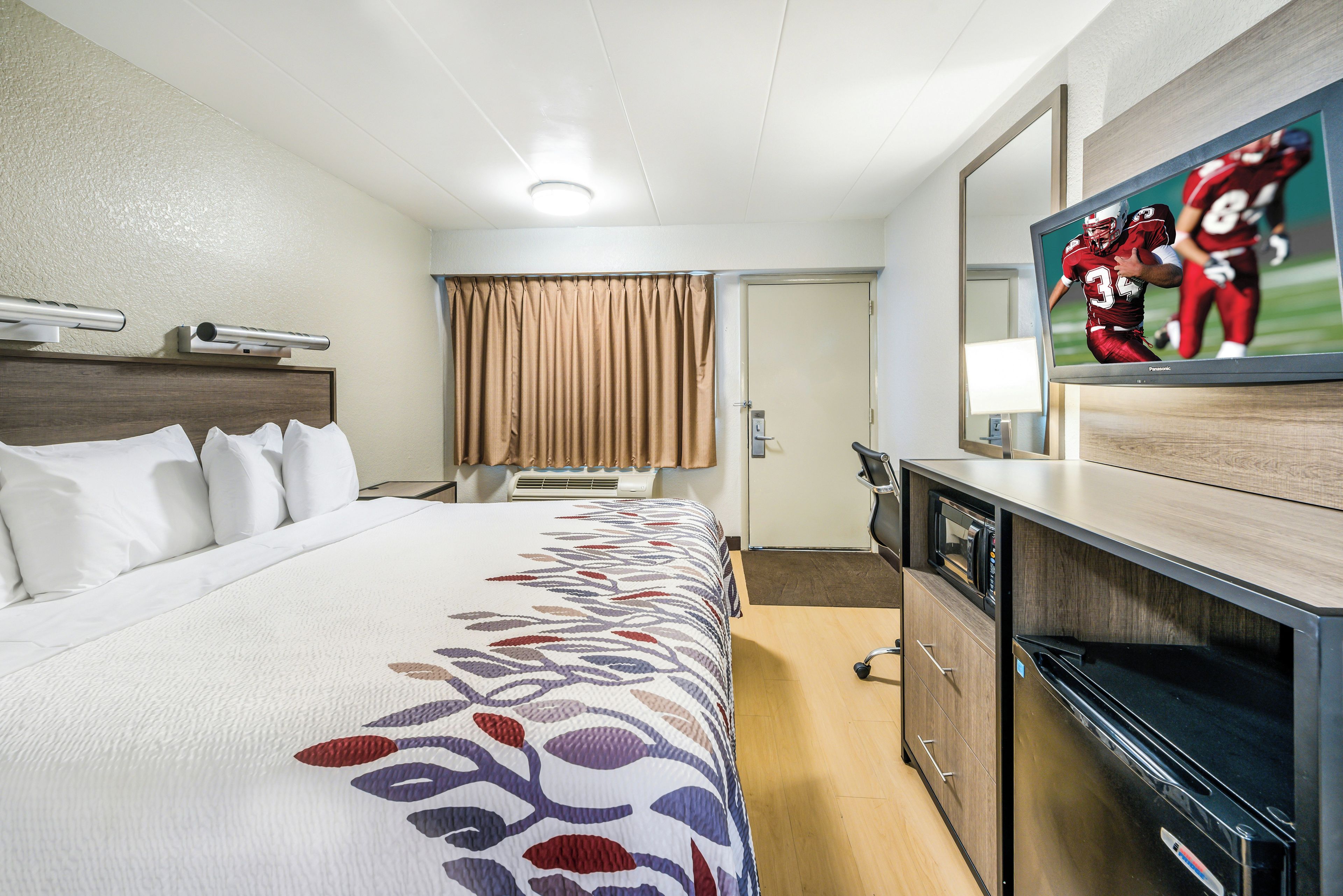 Una habitación de hotel con cama, televisión, escritorio y puerta.