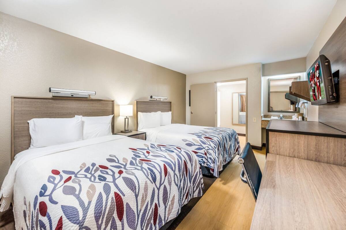 A hotel room with two beds, a desk, a mirror, and a television.