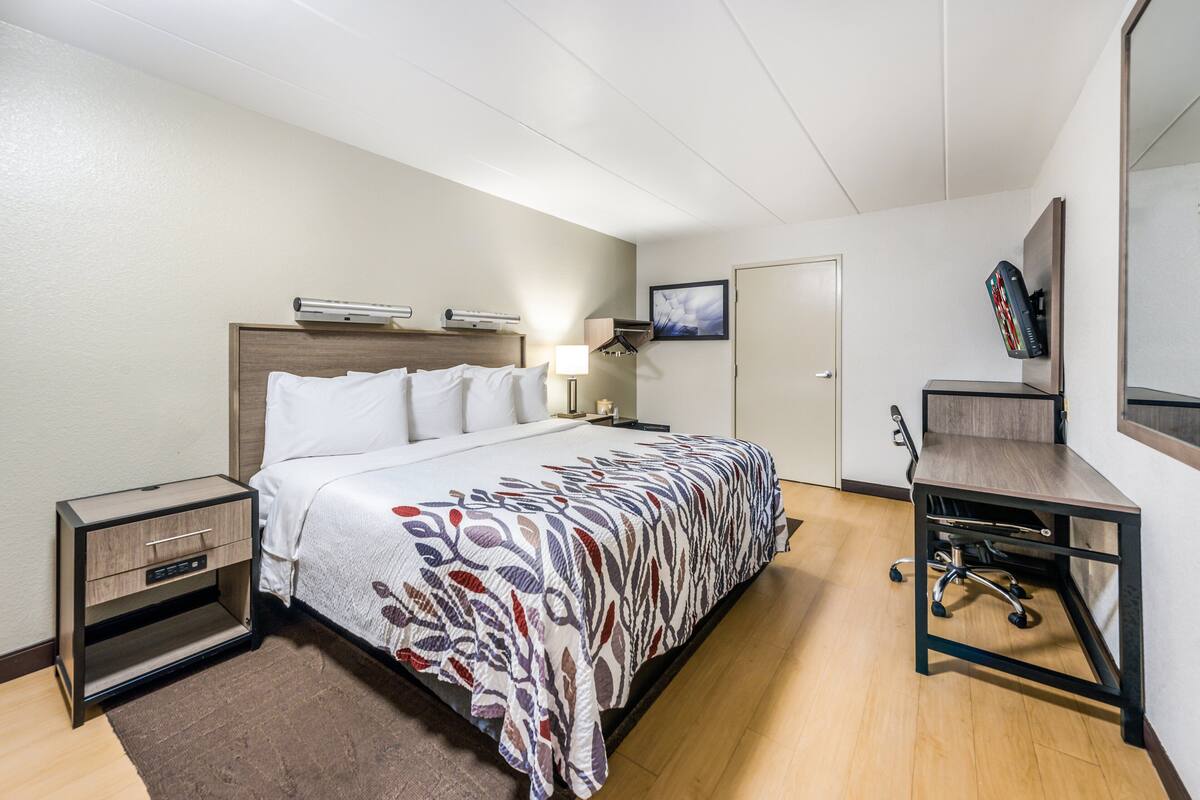 A hotel room with a bed, bedside table, desk, chair, and a door.