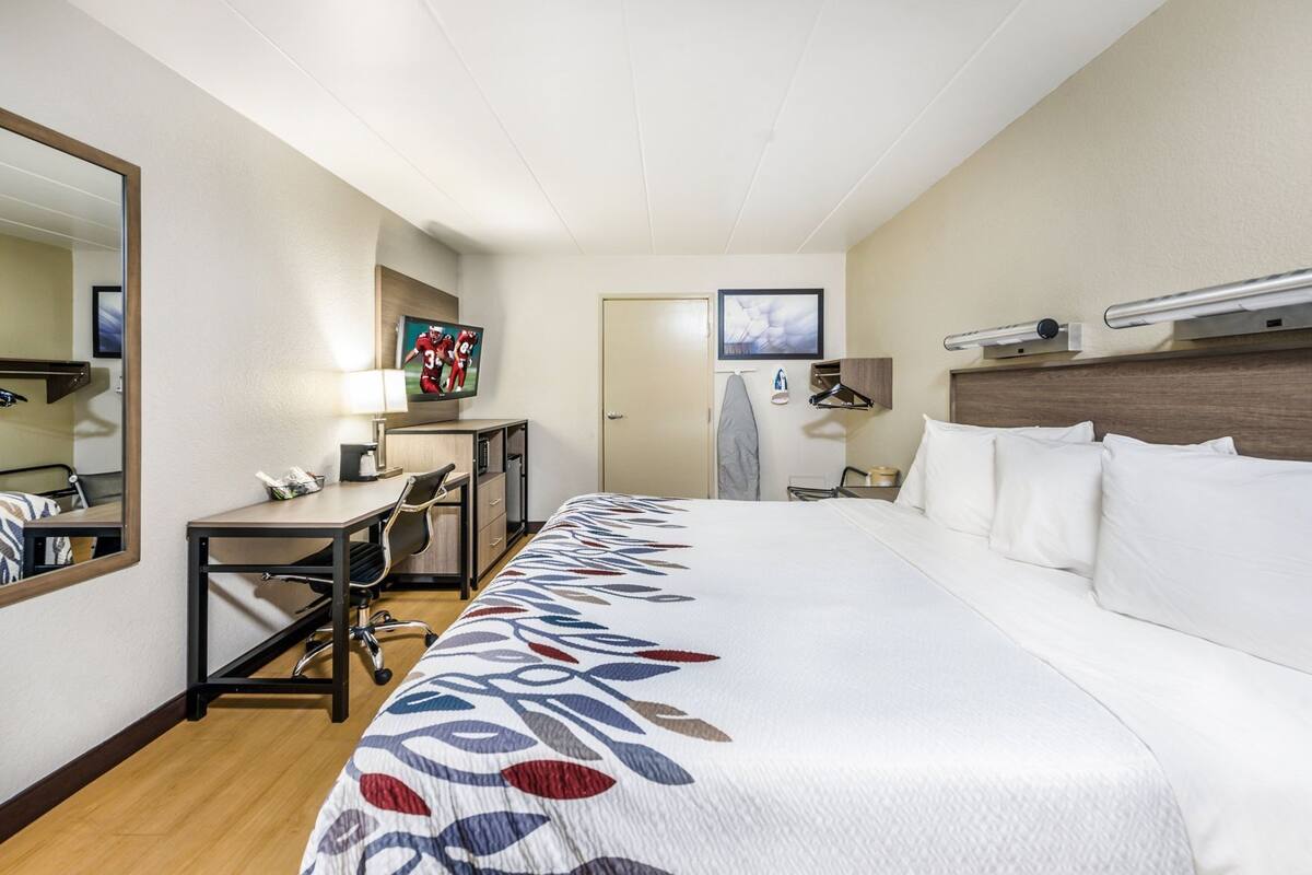 A hotel room with a large bed, a desk with a chair, a TV, a wardrobe, and a mirror.