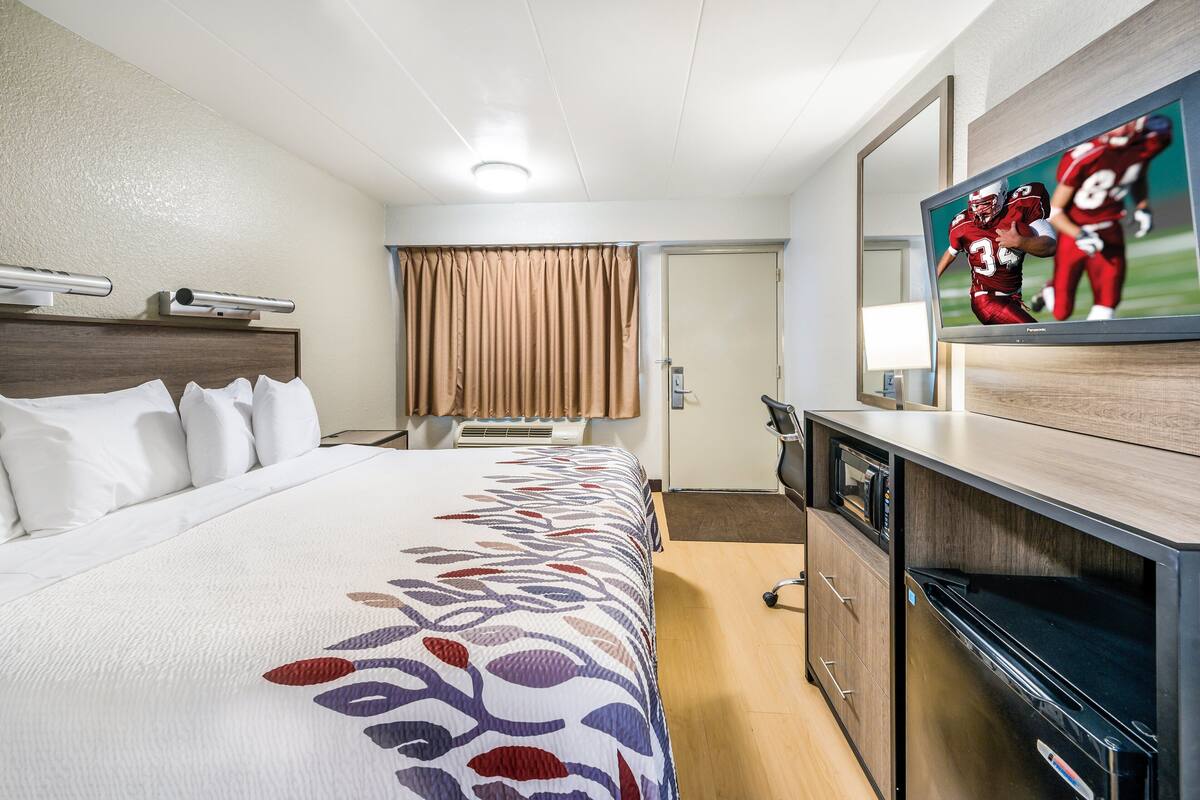 A hotel room with a large bed, a flat-screen TV, a microwave, and a wooden desk.