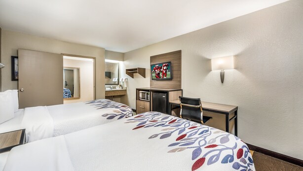 Habitación de hotel con dos camas, un escritorio, un espejo, un televisor y una lámpara fijada a la pared.