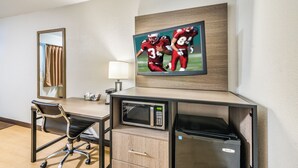 Habitación de hotel con escritorio, una silla, microondas, refrigerador, televisor montado en la pared y espejo.