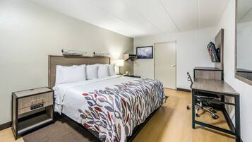 A hotel room with a bed, bedside tables, a desk with a chair, a mirror, and a door.