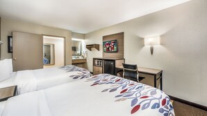 Habitación de hotel con dos camas, un escritorio, un espejo, un televisor y una lámpara de pared.