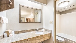 Un baño con encimera de granito, lavamanos, espejo, inodoro y bañera.