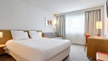 A hotel room with a large bed, a desk, a chair, and a window with curtains.