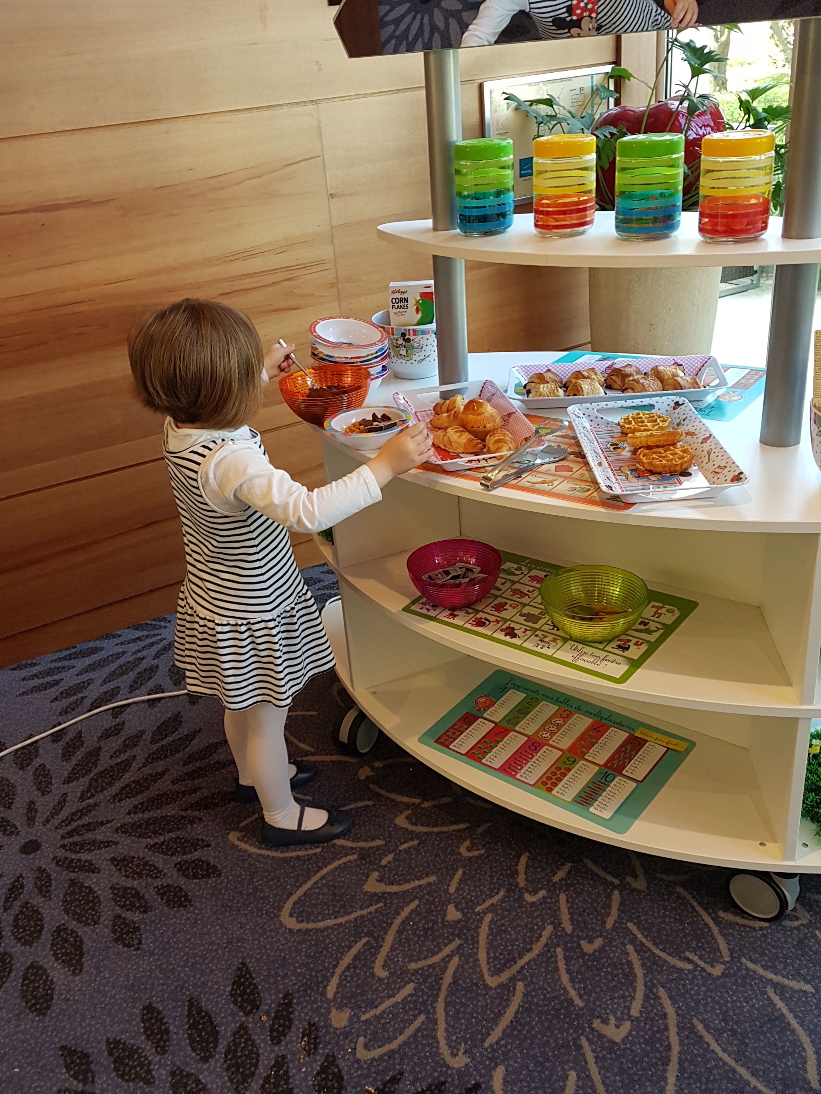 Un enfant tend la main pour attraper de la nourriture sur un plateau tournant où sont disposés divers aliments, comme des céréales, des fruits et des pâtisseries.