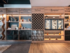A modern retail space with wooden shelving displaying various food items and a refrigerated display case. - Novotel Chartres (Chartres)