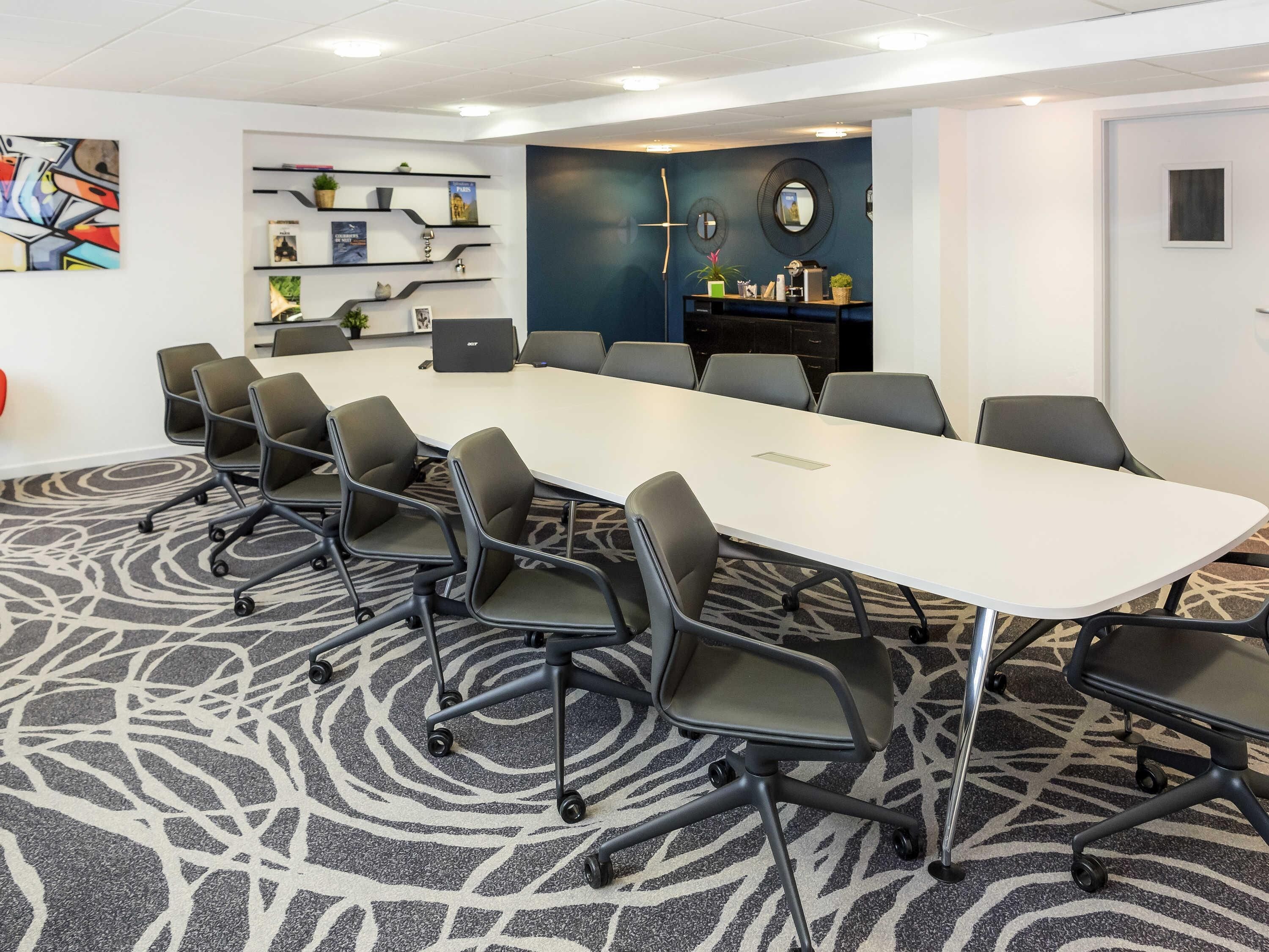 A conference room with a long table, multiple chairs, a laptop, and decorative shelves.
