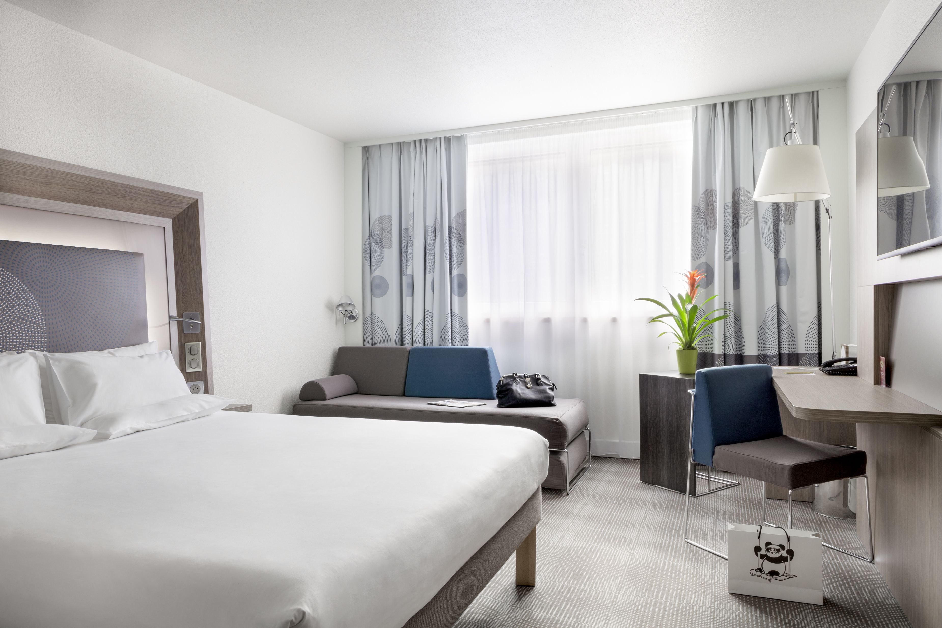 Une chambre d’hôtel avec un grand lit, un bureau, une chaise et une petite table sur laquelle est posée une plante.