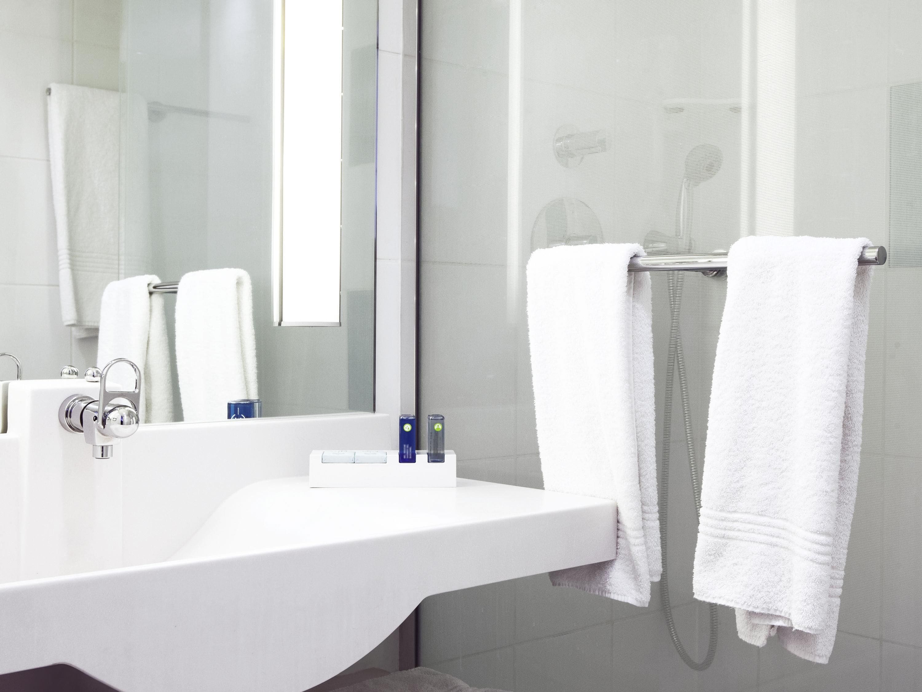 A modern bathroom with a white sink, a mirror, and two white towels hanging on a towel rack.