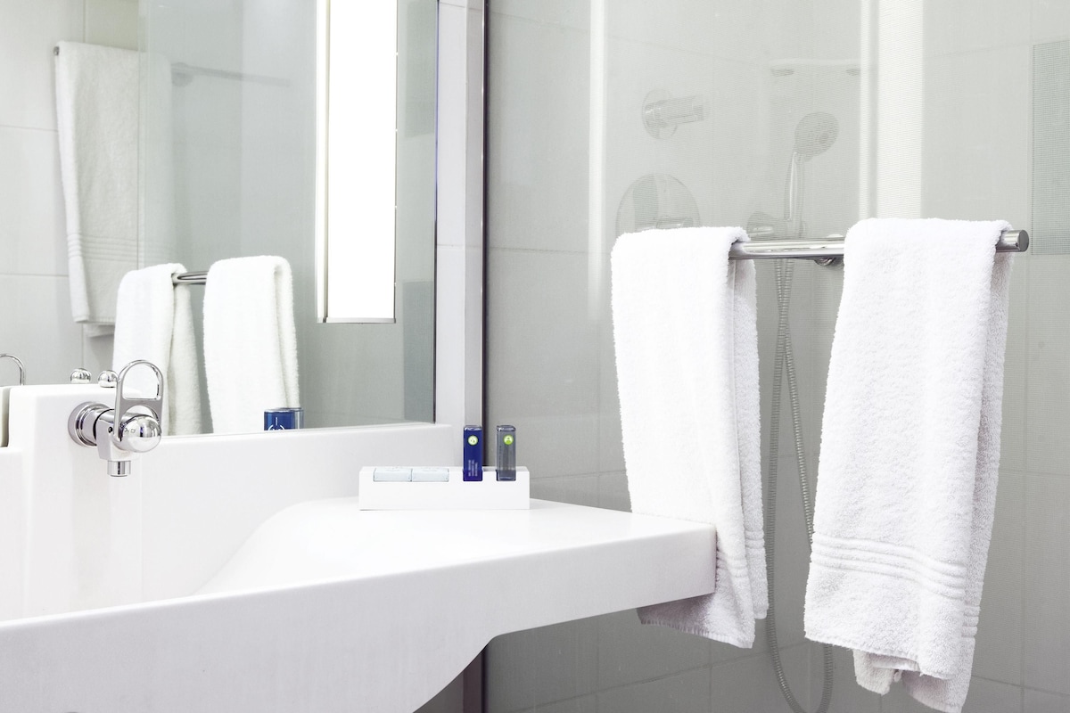 Un baño moderno con un lavamanos blanco, un espejo y dos toallas blancas colgadas en un perchero.