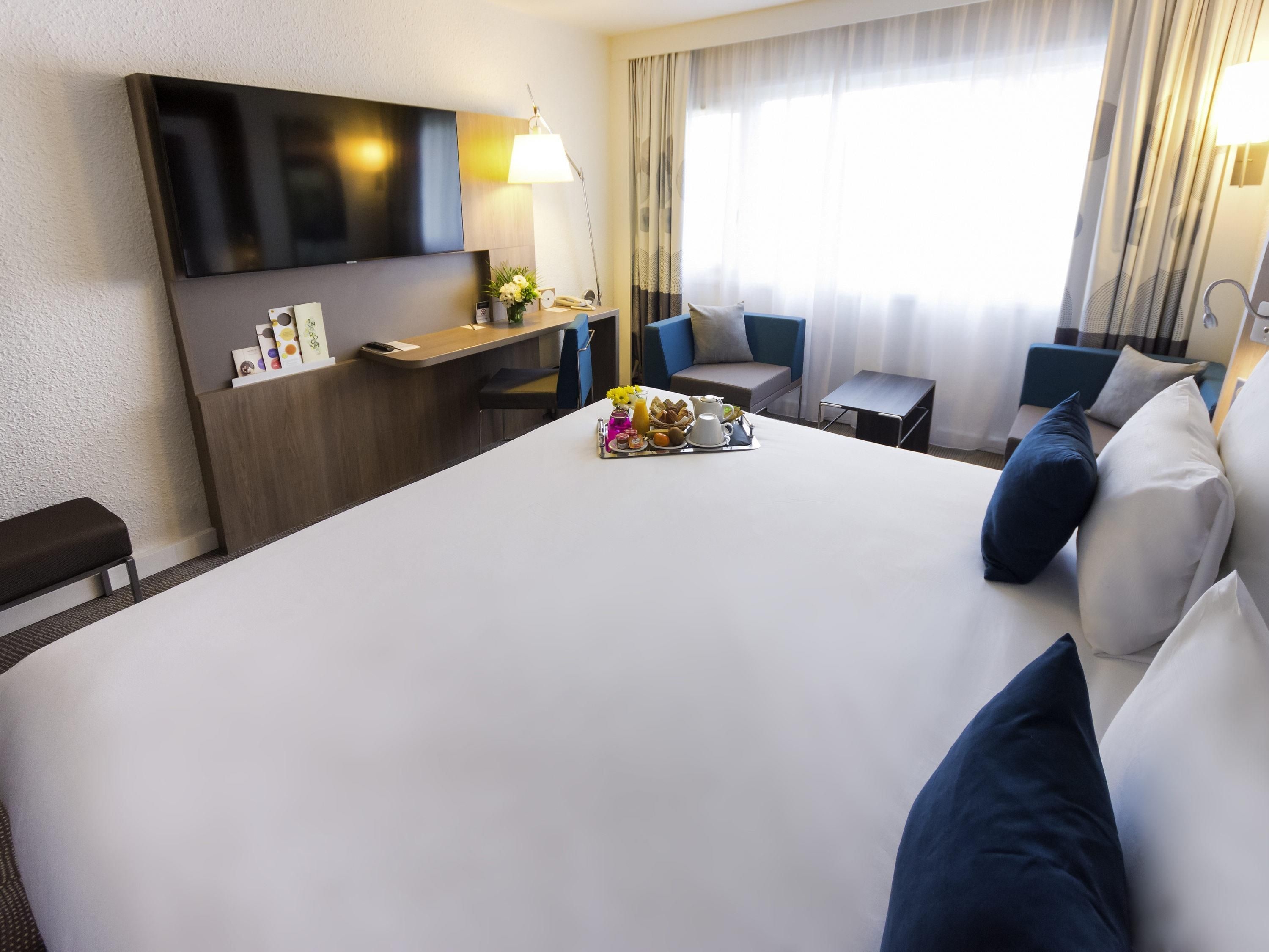 A hotel room with a large bed, a desk with a lamp, a TV, and a window with curtains.