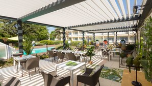 An outdoor patio area with tables and chairs, a pool, and a covered section with umbrellas.