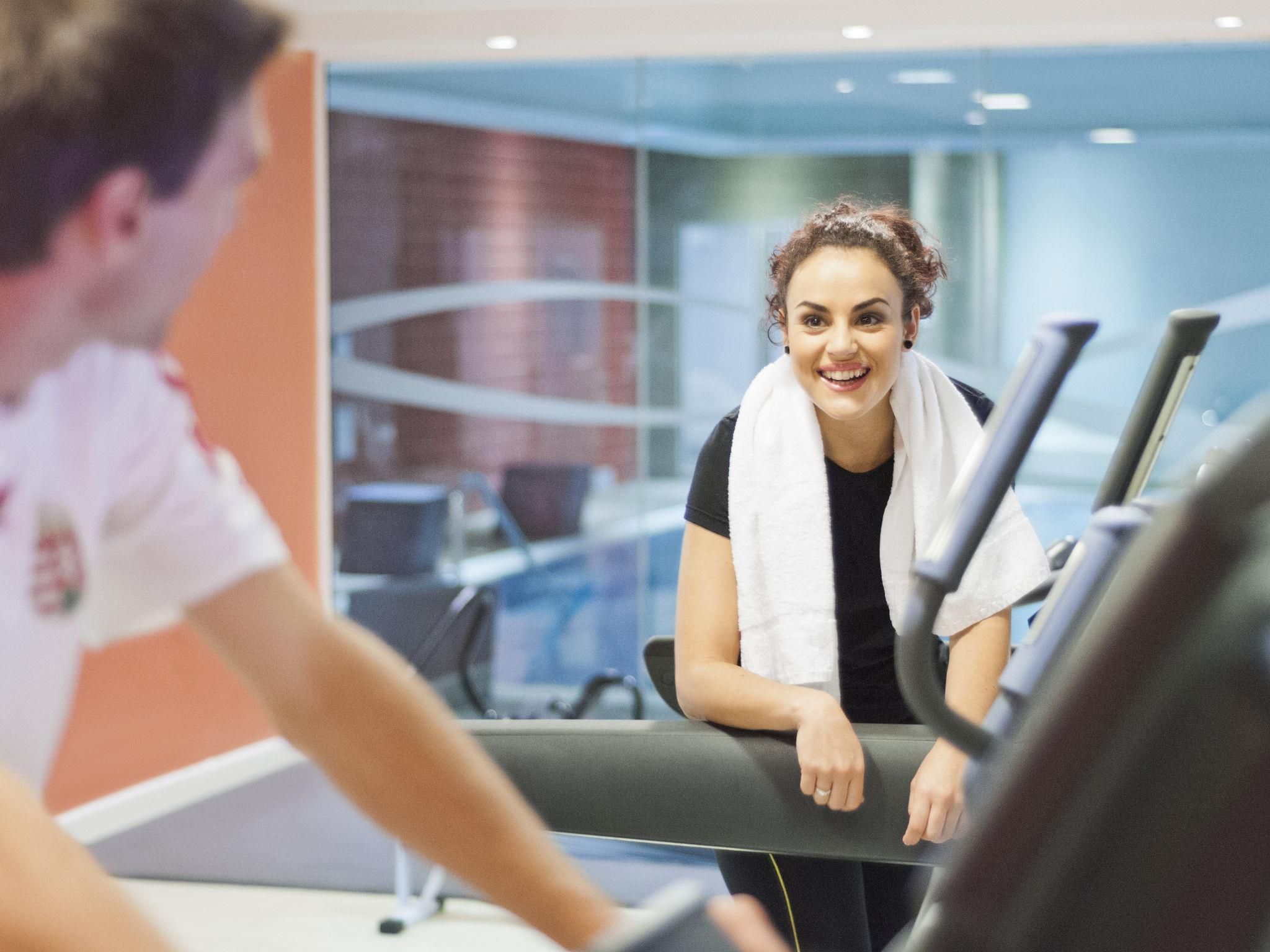 A person using a treadmill in a gym with a modern design, including glass walls and a visible window.