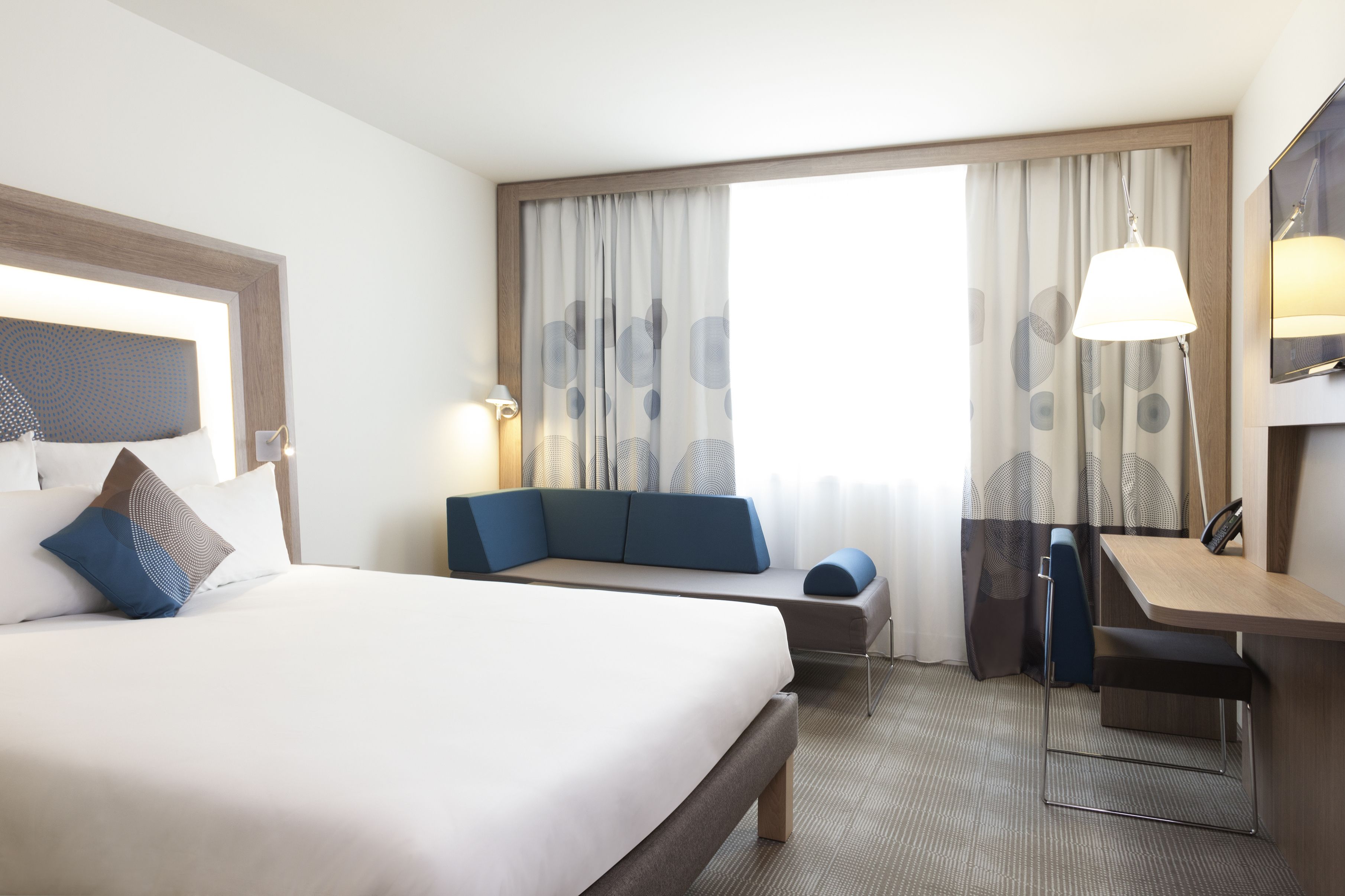 Ett hotellrum med en stor säng, ett skrivbord, en stol, en soffa och ett fönster med gardiner.
