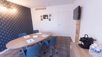 A conference room with a wooden table, blue chairs, a white door, a mounted TV, and a coffee machine.