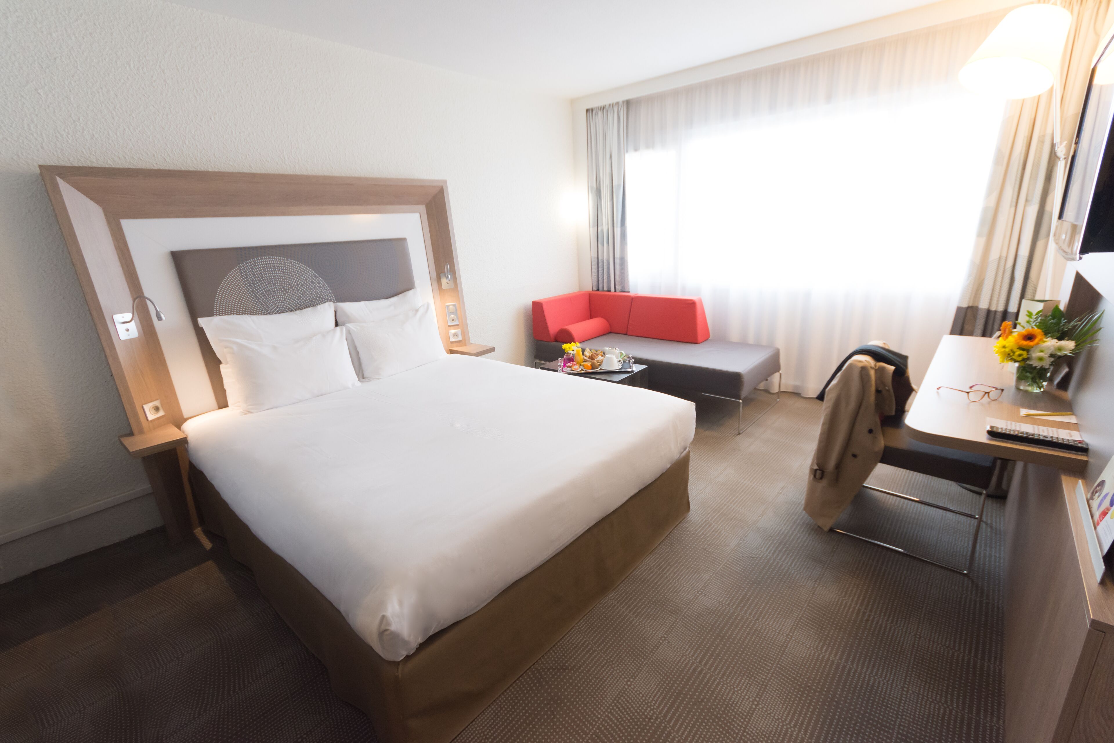 Habitación de hotel con una cama grande, un sofá, un escritorio con lámpara y una ventana con cortinas.