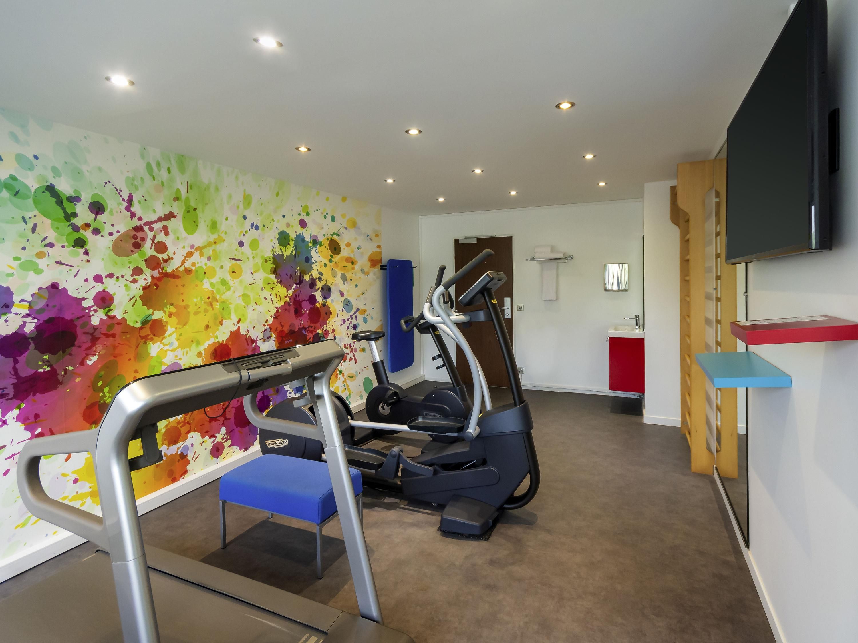 A gym with exercise equipment, a colorful wall, a TV, and a red cabinet.