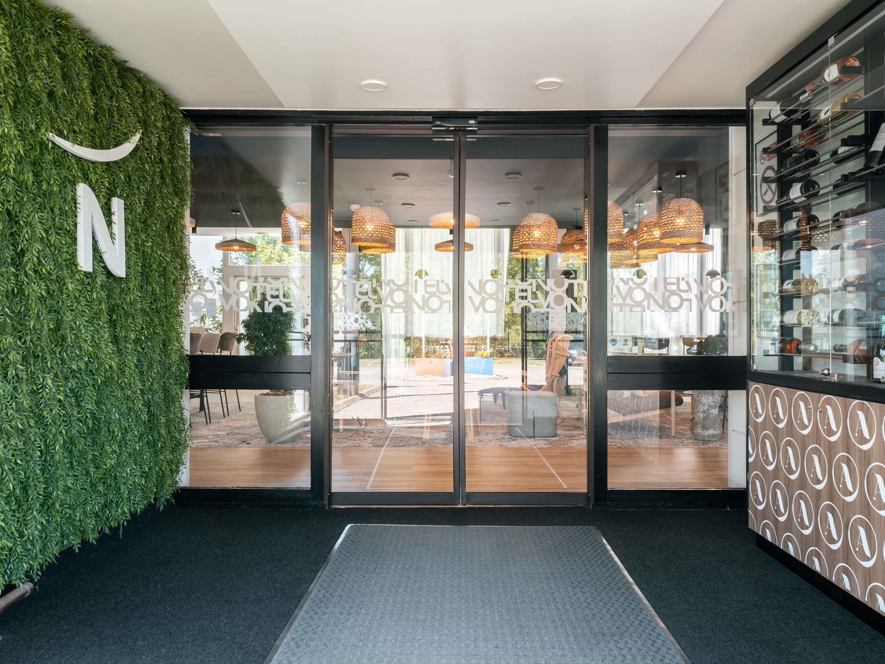 Entrada de hotel con puerta de cristal, pared verde con letrero 'N' y pared con diseño a la derecha.