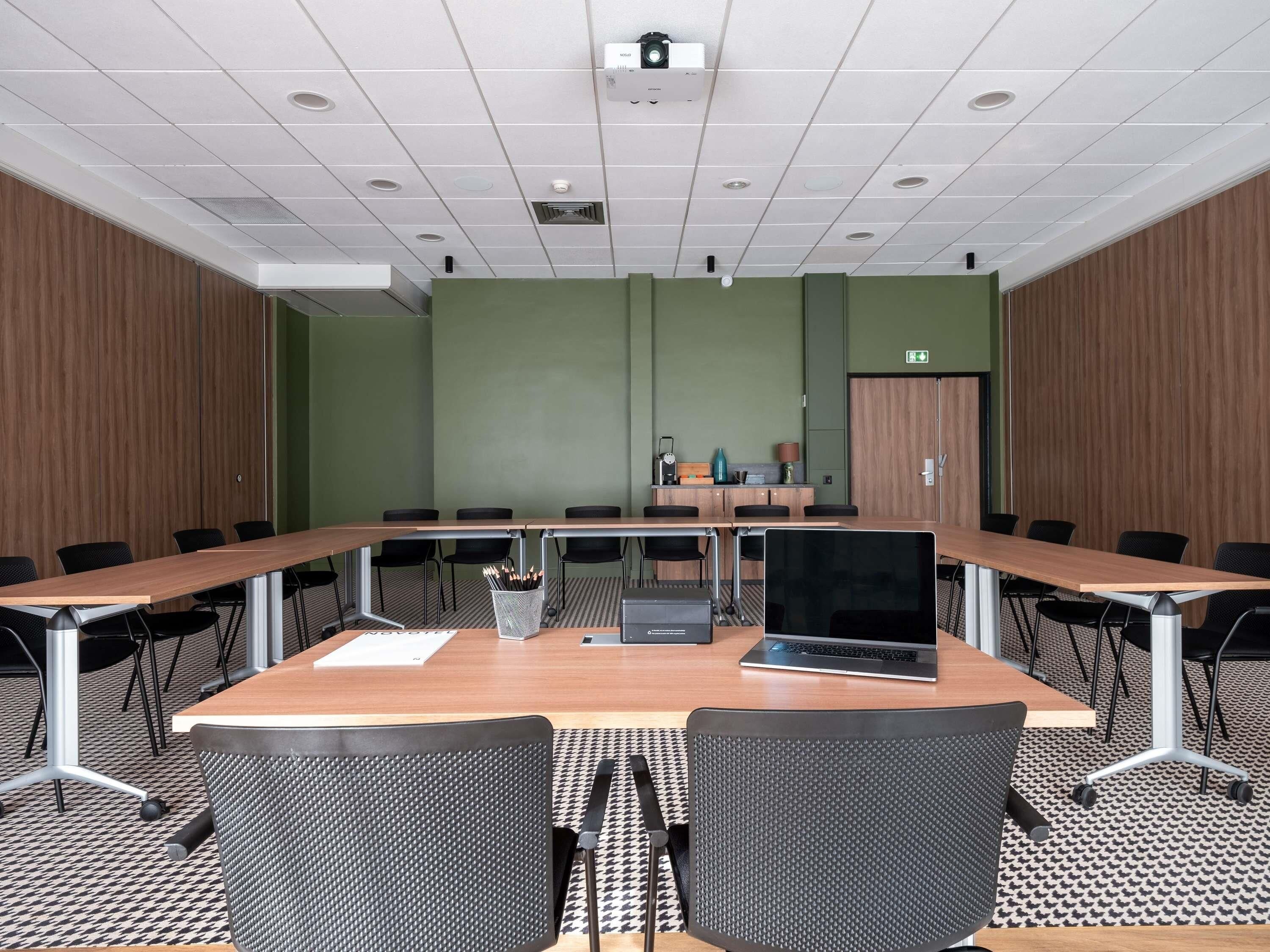 Ein Konferenzraum mit einem langen Tisch, mehreren Stühlen, einem Projektor und einem Laptop.