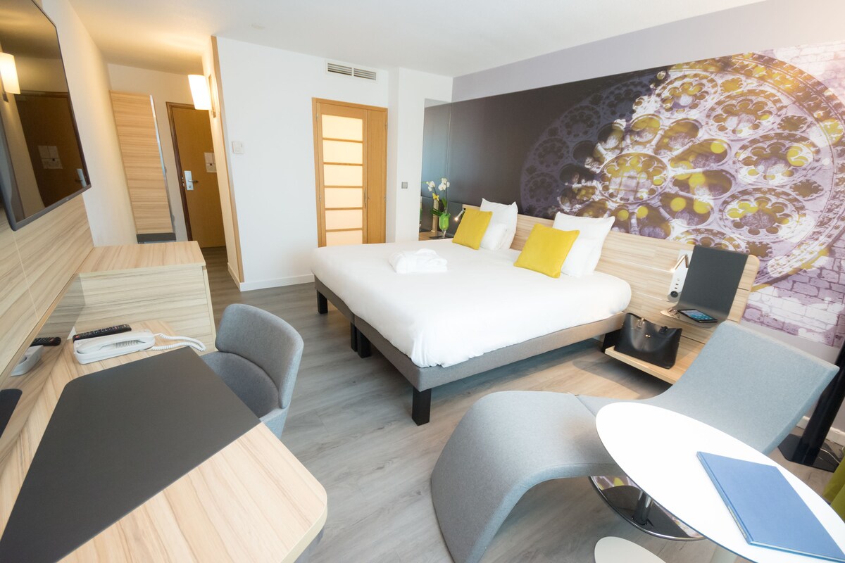 A hotel room with a bed, a desk, a chair, and a TV.
