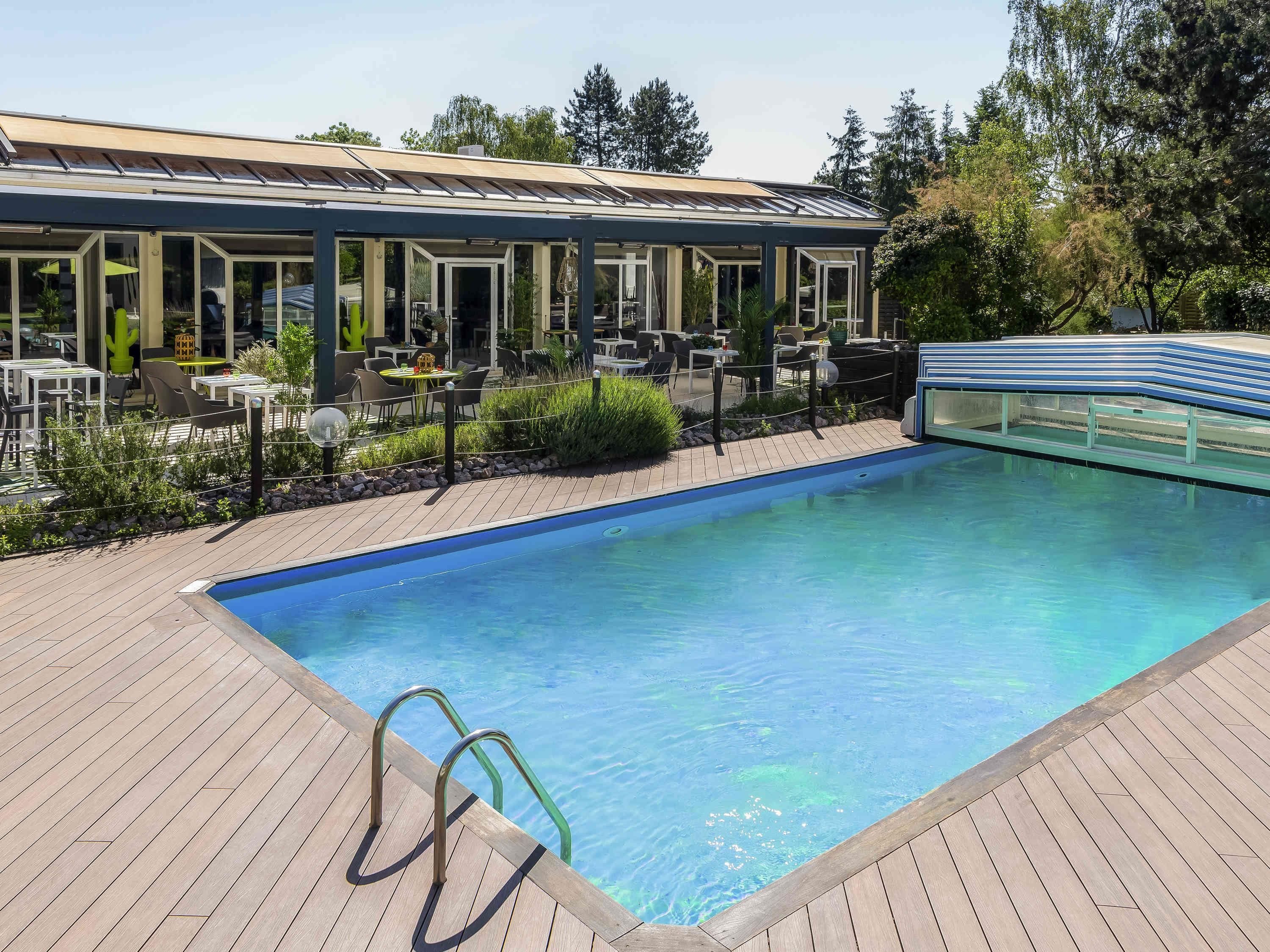 A pool area with a wooden deck, a glass-enclosed lounge, and outdoor seating.