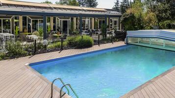A pool area with a wooden deck, a glass-enclosed lounge, and outdoor seating.
