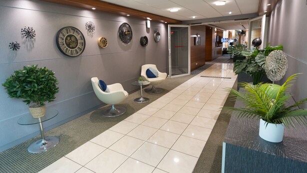 A reception area with a modern design, featuring a reception desk, two seating areas with chairs, and decorative wall clocks.