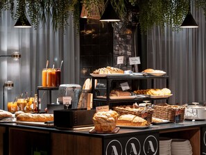 A breakfast buffet with various breads, pastries, and beverages.