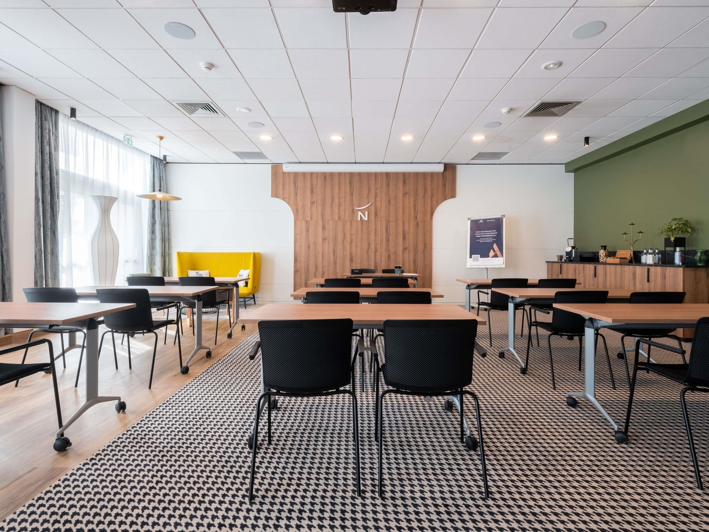 A modern conference room with a large table, black chairs, a patterned carpet, and a wooden accent wall.