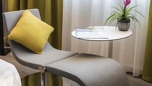 A modern lounge chair with a metallic base, a yellow cushion, and a small table with a book and a potted plant.