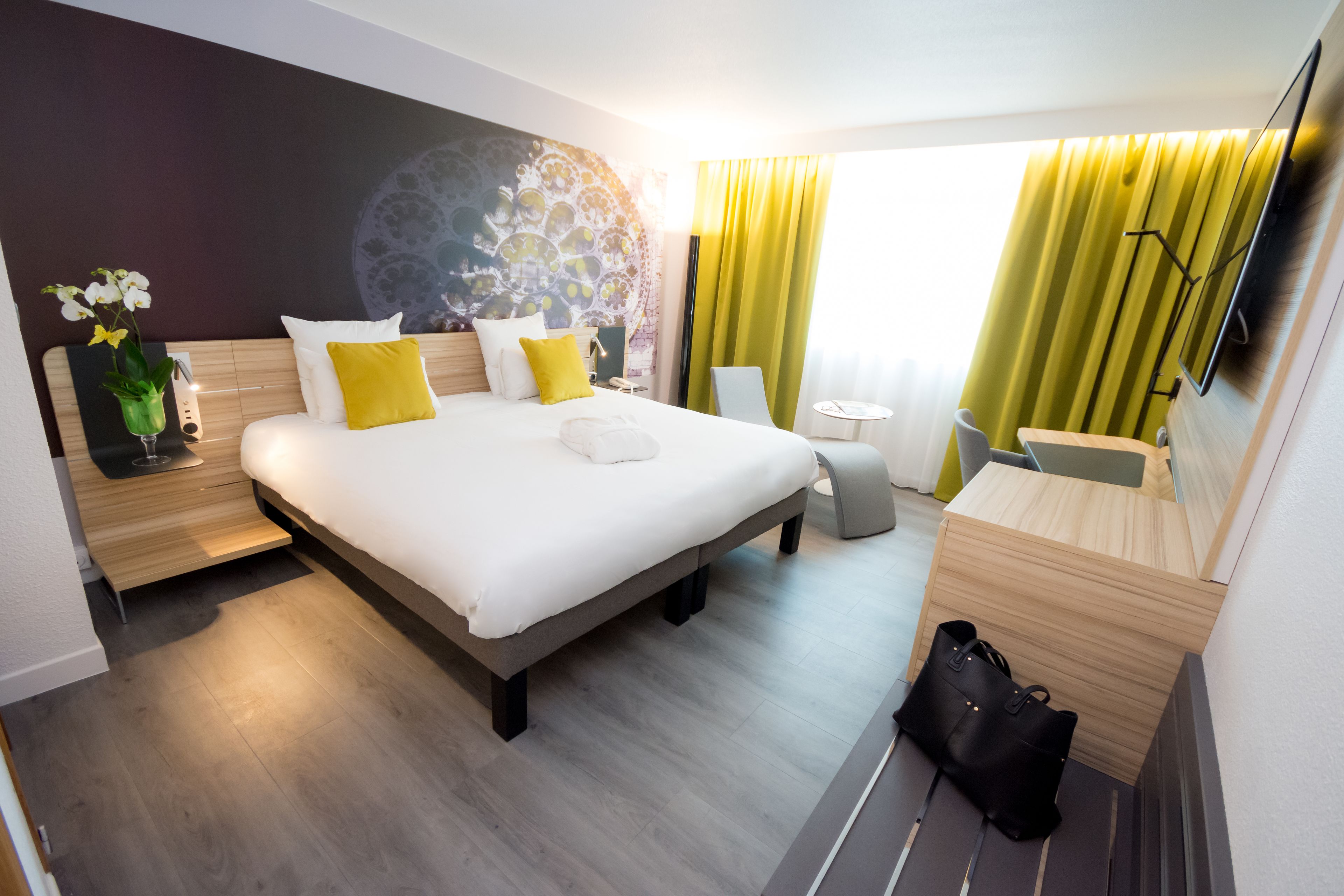 A modern hotel room with a large bed, a desk, a chair, and a TV.