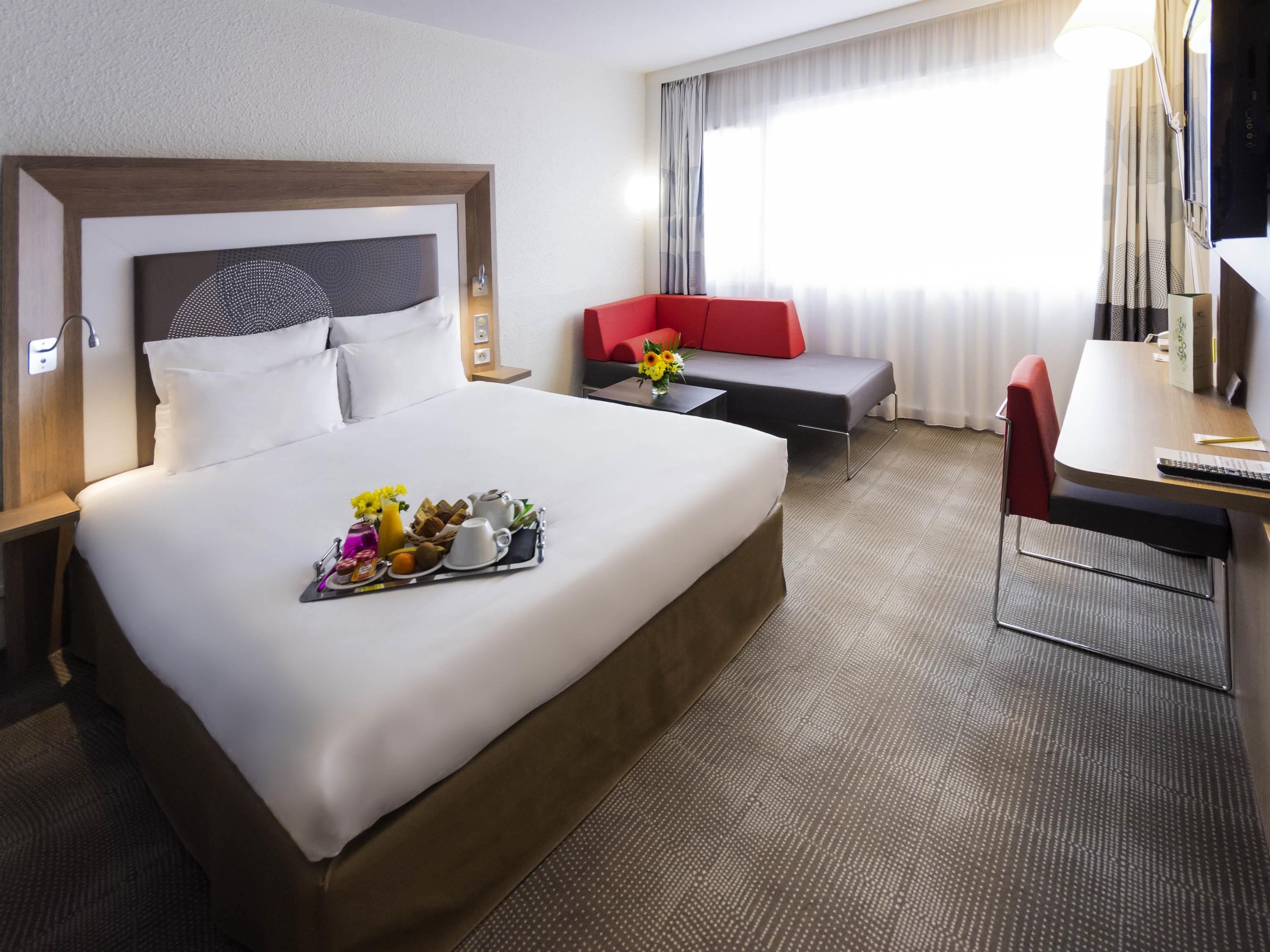 A hotel room with a large bed, a desk, a red sofa, and a TV.