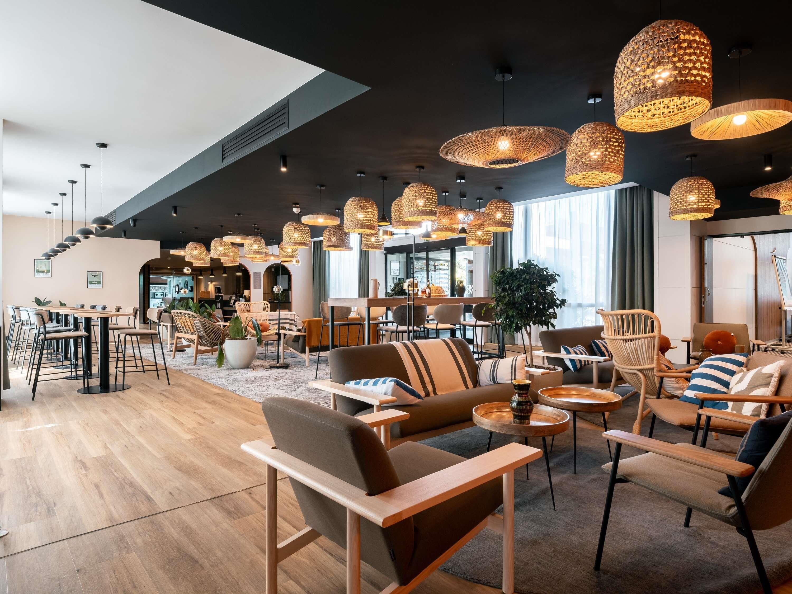 A modern lounge area with wooden flooring, comfortable seating, and multiple hanging wicker lamps.
