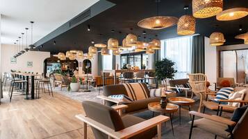 A modern lounge area with wooden flooring, comfortable seating, and multiple hanging wicker lamps.