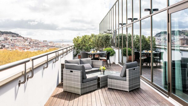 A balcony with wicker furniture, a table, and chairs, overlooking a cityscape. - Sofitel Lisbon Liberdade (Lisbon)